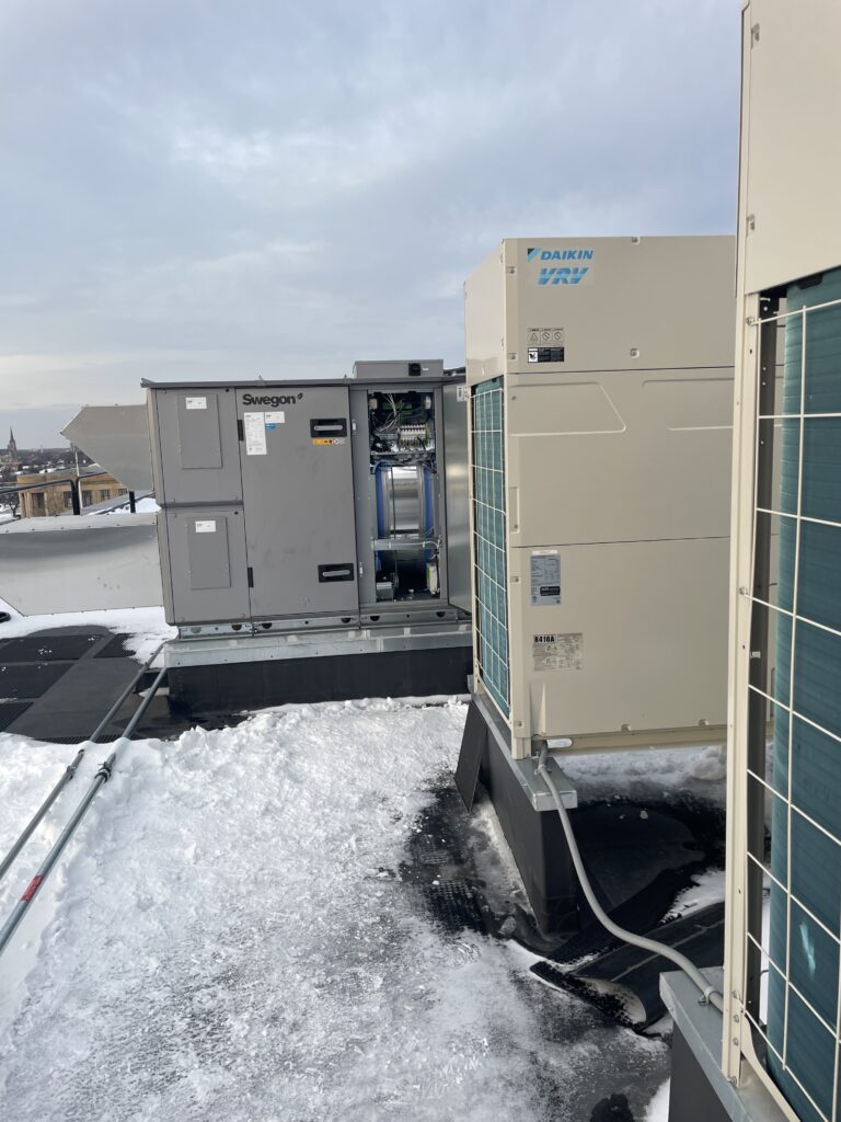 Daikin VRV outdoor unit and Swegon ventilation unit installed on a commercial rooftop in winter, with snow surrounding the equipment.